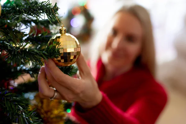 クリスマスの時期に彼女の居間でクリスマスツリーを飾る笑顔の若い白人女性の正面図 — ストック写真