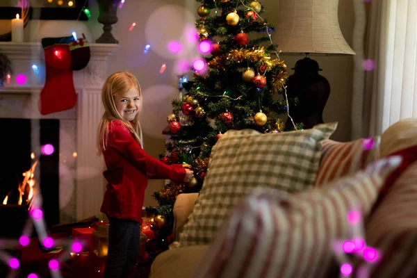 クリスマスの時期に居間にクリスマスツリーを飾る若い白人の女の子の側面図 — ストック写真
