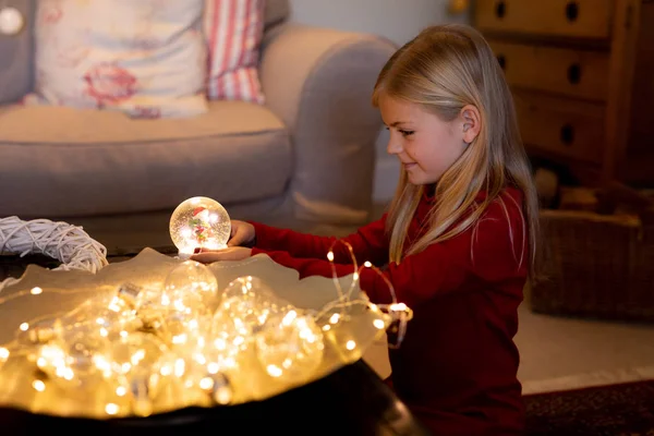 クリスマスの時期に居間に雪の球体を持つ若い白人の女の子の側面図 — ストック写真