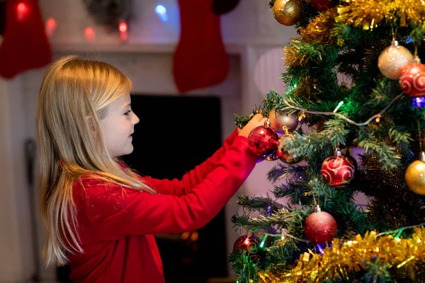圣诞节时 一个年轻的白种女孩在客厅里装饰圣诞树的侧视图 — 图库照片