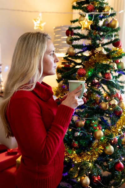 圣诞节时 一位年轻的白种妇女在她的客厅里拿着一个杯子的侧视图 — 图库照片