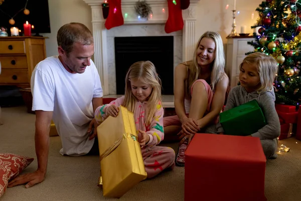 圣诞节时 一对白种人夫妇坐在地板上 带着年幼的儿子和女儿坐在客厅里 打开礼物 面带微笑 — 图库照片
