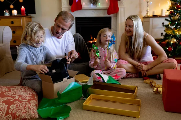 クリスマスの時に自分の居間で幼い息子と娘と一緒に床に座っている白人カップルの正面図 プレゼントを開き — ストック写真