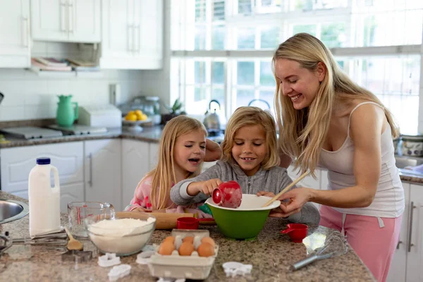 圣诞节时 一个快乐的年轻白种人母亲带着年幼的女儿和儿子在厨房里做饼干 手里拿着一个混合碗 加入配料 面带微笑 — 图库照片