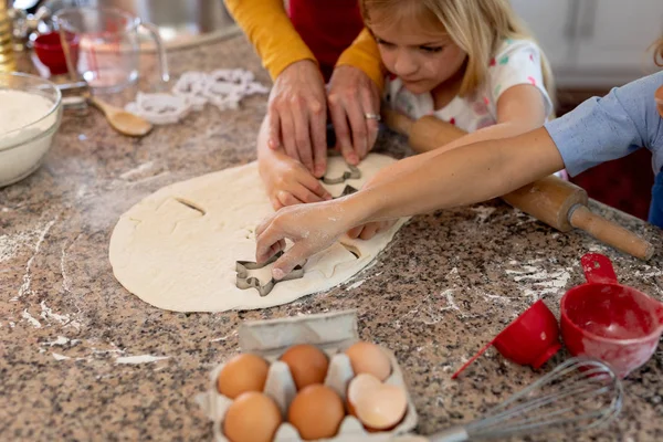 一个快乐的高加索女孩用她的母亲和兄弟的手 在圣诞节的时候忙着在厨房里做饼干 用面团切饼干的样子 在镜头前走近一个快乐的白人女孩 — 图库照片