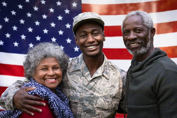 一个年轻的非裔美国士兵和他的父母拥抱在一起的画像 他们都在一面美国国旗前微笑着拍照 — 图库照片