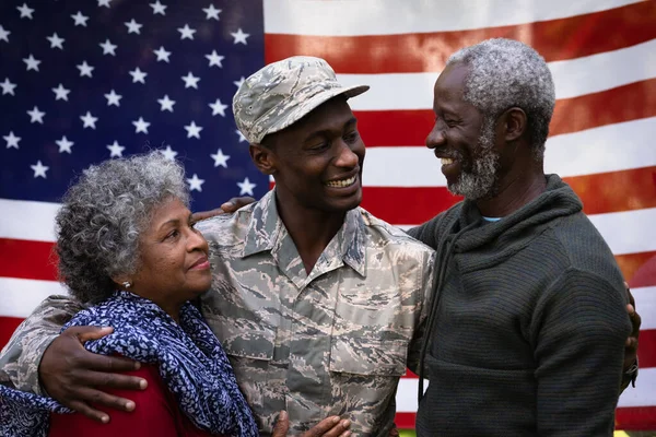一个年轻的非裔美国士兵和他的父母拥抱在一起 在一面美国国旗前互相微笑的画像 — 图库照片