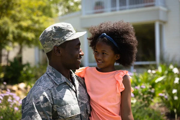 一位年轻的非裔美国士兵在自家门外的花园里 抱着他的小女儿 面带微笑地望着对方 眼前的景象非常逼真 — 图库照片