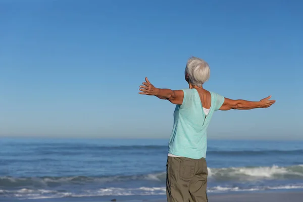 在阳光明媚的日子里 白种人的老妇人在海滩上尽情享受时光 张开双臂 背对着大海微笑 — 图库照片