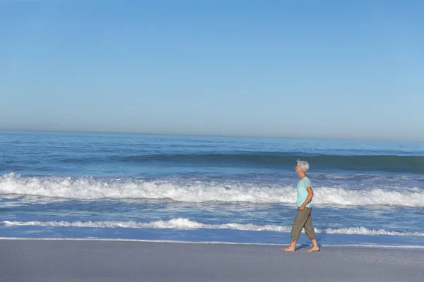 晴れた日にビーチで時間を楽しむシニア白人女性 背景に海と歩いて — ストック写真
