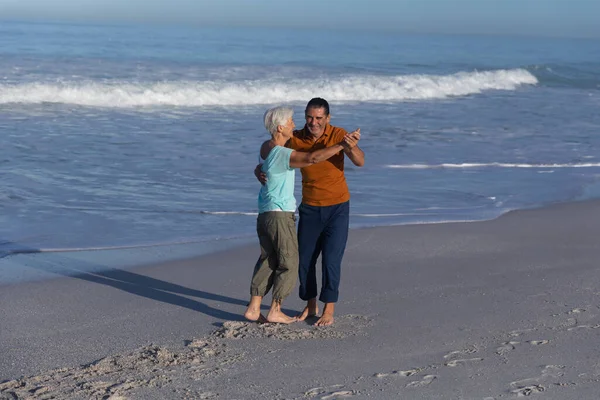 在阳光明媚的日子里 白种人的一对老夫妻在海滩上欢度时光 光着脚与大海共舞 — 图库照片