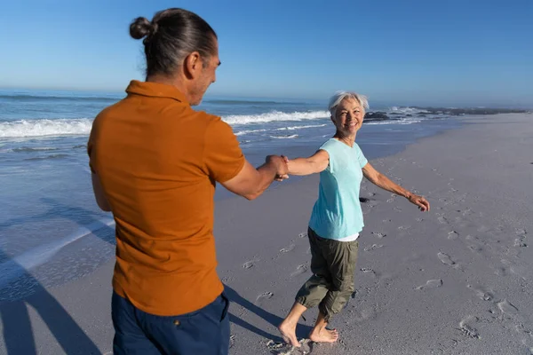 晴れた日にビーチで時間を楽しんでいるシニア白人カップル 背景に海と歩いて手を取り合って — ストック写真