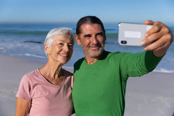 在阳光明媚的日子里 白种人的一对老夫妻在海滩上享受着时光 他们抱着自己 背对着大海自拍 — 图库照片