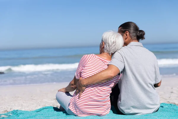 在阳光明媚的日子里 白种人的一对老夫妻在海滩上享受时光 他们坐在毛毯上 背对着大海 — 图库照片