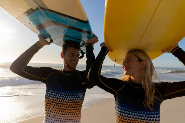 白人夫婦は晴れた日にビーチで時間を楽しみ 背景に海と一緒に頭の上にサーフボードを保持しています — ストック写真