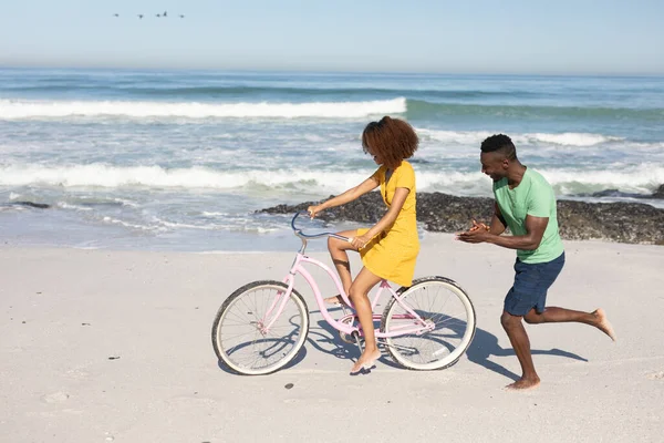 在阳光灿烂的日子里 一对混血的夫妇一起在海滩上享受着闲暇时光 骑自行车 脸上闪烁着欢乐的光芒 — 图库照片