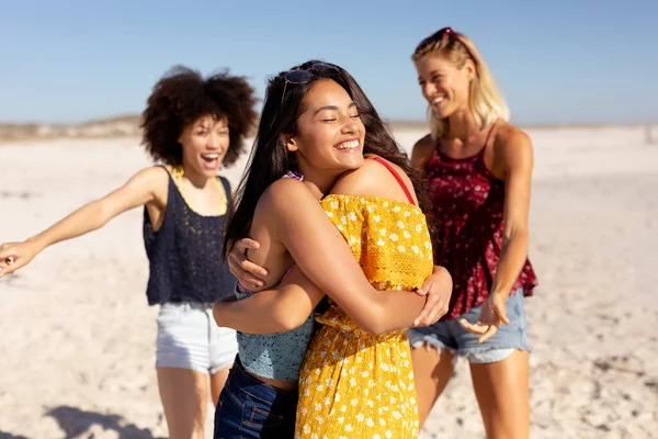 由4名成年女性组成的多民族团体在阳光普照的海滩上相遇 在蓝天和沙滩的衬托下 拥抱和欢笑着 — 图库照片