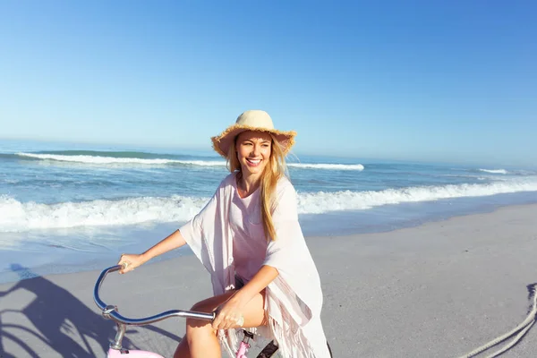 晴れた日にビーチで時間を楽しむ帽子をかぶった白人女性 自転車に乗って 背景に海があります — ストック写真