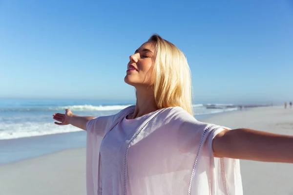 一个白种人女人在阳光灿烂的日子里享受着海滩上的时光 张开双臂 背对着大海微笑 — 图库照片