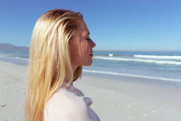 在一个阳光明媚的日子里 一位白种人女人站在海滩上 闭着眼睛 背对着大海 正在享受她的美好时光 — 图库照片