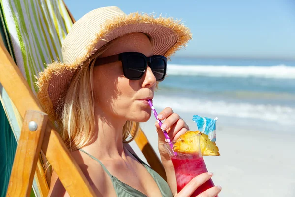晴れた日にビーチで時間を楽しんで帽子をかぶっている白人女性のクローズアップ デッキチェアに座って カクテルを飲みます — ストック写真