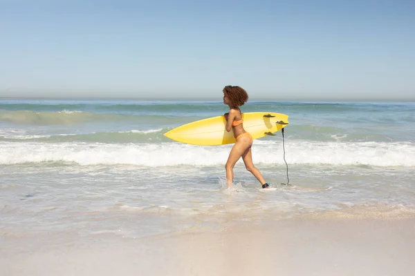 晴れた日にビーチで自由な時間を楽しむ魅力的な混合レースの女性 水着を着て サーフィン 彼女のサーフボードを運ぶ — ストック写真