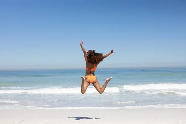 在阳光明媚的日子里 她穿着泳衣 抱着升起的太阳光在空中跳跃 享受着沙滩上的闲暇时光 — 图库照片