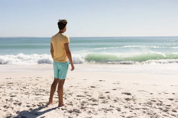 素足で立って波を見ながら 晴れた日に彼の友人と一緒にビーチで彼の時間を楽しんで白人男性 — ストック写真