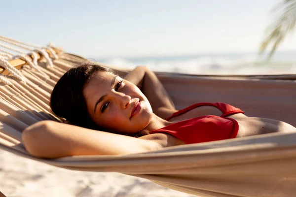 在阳光灿烂的日子里 白种人女人在海滩上享受着自己的时光 躺在吊床上晒日光浴 看着相机 面带微笑 — 图库照片