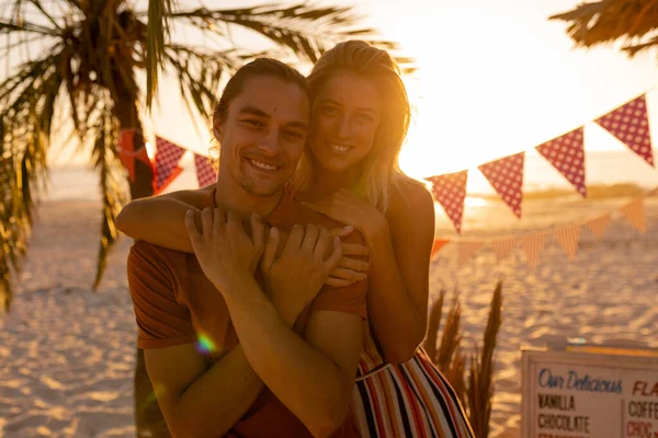 白人男性と女性は 夕日の間にビーチでの時間を楽しんで カメラを見て笑顔で抱き合って — ストック写真