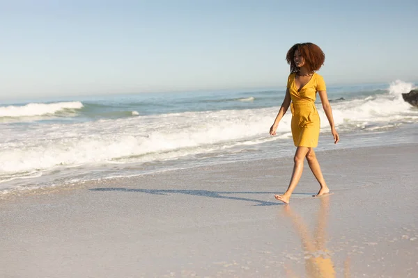 幸せな魅力的な混合レースの女性は 晴れた日にビーチで無料の時間を楽しんで 黄色のドレスを着て 歩いて — ストック写真