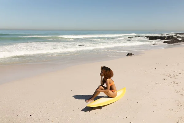 在阳光灿烂的日子里 一位迷人的混血女子坐在冲浪板上 尽情享受沙滩上的闲暇时光 — 图库照片