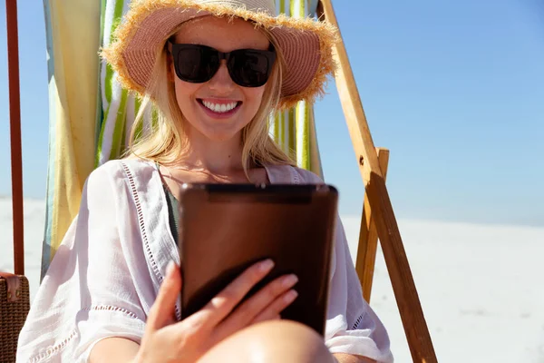 晴れた日にビーチで時間を楽しむ魅力的なブロンドの白人女性 デッキチェアに座って タブレットコンピュータを使用して 背景に青い空と海と 夏の熱帯のビーチ休暇 — ストック写真