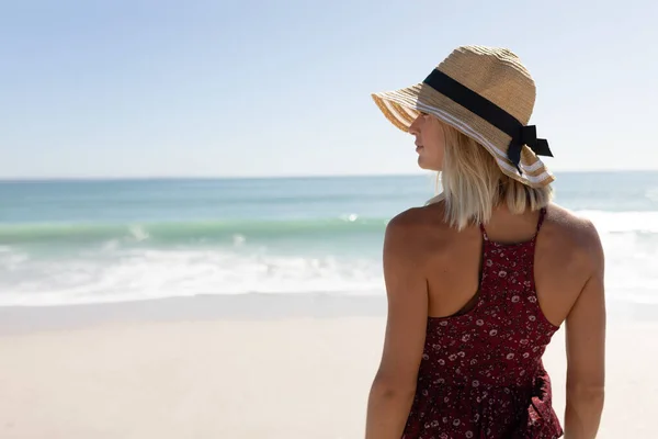 金发白种人女人戴着草帽 享受着在一个田园诗般的阳光普照的海滩上散步的闲暇时光 背景是蓝天和大海 放宽热带海滩假期 — 图库照片