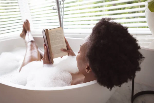 混合人種の女性は自宅で時間を費やしています自己隔離と社会的距離で隔離されたロックダウン中にコロナウイルスCovid 19流行 泡立ちの良い 暖かいお風呂を取ります リラックスした 本を読む — ストック写真