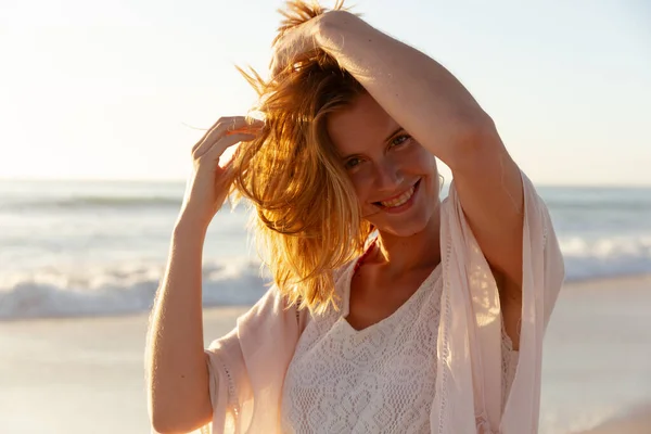 魅力的なブロンドの白人女性は 日没時にビーチで時間を楽しんで カメラを見て笑顔で 背景に夕日の空と海と 夏の熱帯のビーチ休暇 — ストック写真