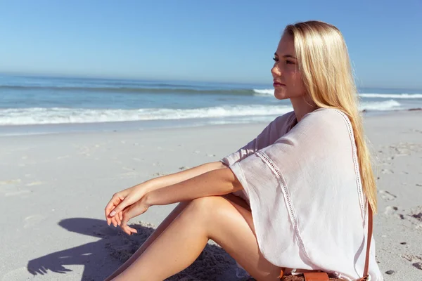 魅力的なブロンドの白人女性は 晴れた日にビーチで時間を楽しんで 座って遠くを見て 青い空と海を背景にしています 夏の熱帯のビーチ休暇 — ストック写真