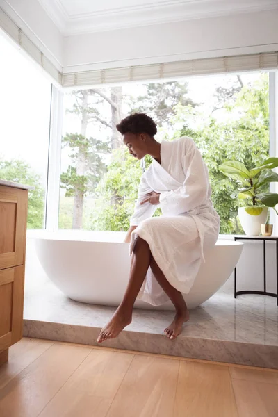 男女混血的女人在自己家里度过了一段自我隔离的时光 她们穿着睡衣坐在浴室的浴池里 在科罗纳维病流行期间处于隔离状态 与外界保持距离 — 图库照片