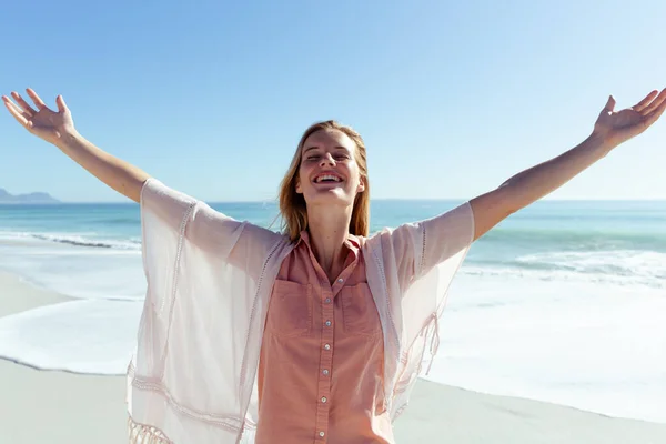 迷人的金发白种女人在阳光灿烂的日子里 在海滩上尽情享受着时光 张开双臂 微笑着 背景是蓝蓝的天空和大海 夏季热带海滩假期 — 图库照片