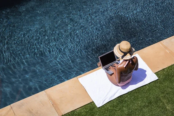 混合レースの女性は ラップトップを使用して 自宅で時間を過ごし プールでリラックスして日光浴をします コロナウイルスの間の隔離されたロックダウンでの自己隔離と社会的距離は19の流行をCovid — ストック写真
