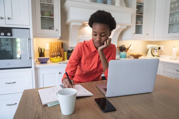 混合人種の女性は自宅で時間を過ごします 彼女の台所でテーブルに座って 彼女のラップトップを使用して作業します自己隔離と社会的距離で隔離されたロックダウン中コロナウイルスCovid 19流行 — ストック写真
