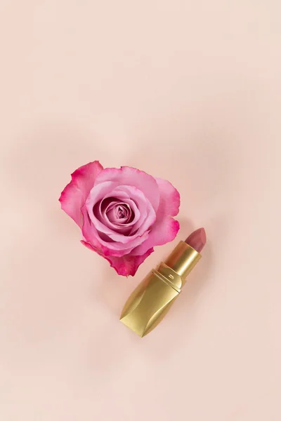 近景的粉色口红在一个金色的管 粉红色的玫瑰设置在一个普通的粉红色的背景 — 图库照片