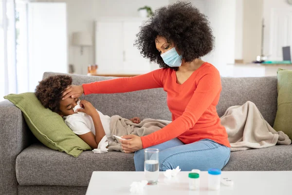 stock image Mixed race mother with son enjoying family time together at home, social distancing and self isolation in quarantine lockdown, boy is lying on couch, wiping his nose with a tissue, woman is sitting by