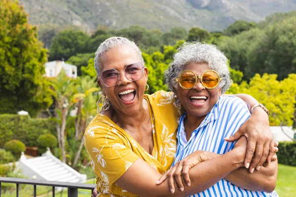 Senior African American woman and senior biracial woman share a joyful embrace outdoors.