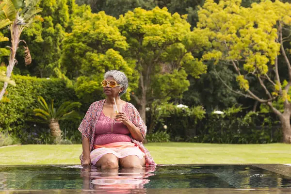 Senior Biracial Woman Gray Hair Relaxes Pool Holding Glass Copy — Stock Photo, Image