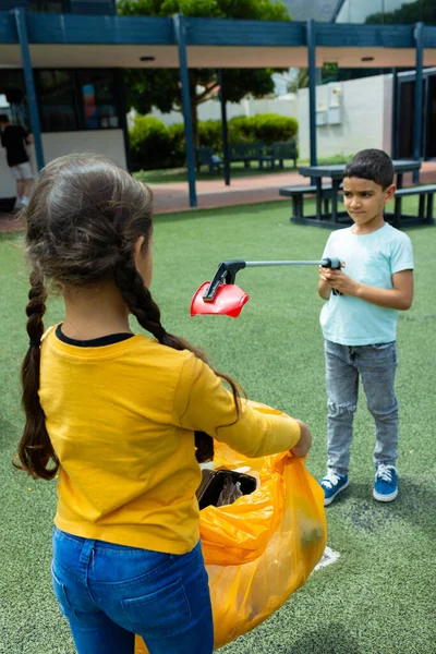 一个留着辫子的女孩拿着垃圾袋 一个捡垃圾的男孩 他们白天在学校操场上打扫卫生 — 图库照片