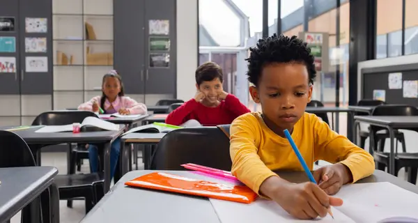 Biracial Boy Žlutém Zaměřuje Psaní Stolem Školní Třídě Nastavení Učeben — Stock fotografie