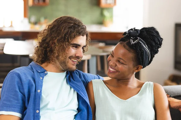 Diverse couple, young African American woman and Caucasian man share a joyful moment on the couch. Her hair is adorned with a headband, and his curly brown locks complement his casual blue shirt.