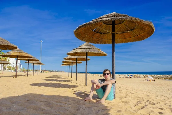 Ein Teenager sitzt unter einem Schilfschirm am Strand — Stockfoto