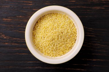 Organic millet seeds in a ceramic bowl on wooden black rustic table. Millet can be used to a gluten-free diet.Close up view.